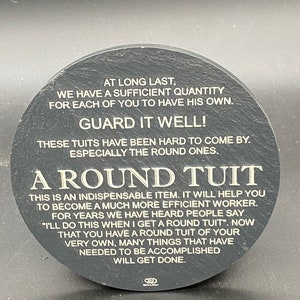 May include: A round black coaster with white text that reads "At long last, we have a sufficient quantity for each of you to have his own. Guard it well! These tuits have been hard to come by. Especially the round ones. A Round Tuit. This is an indispensable item. It will help you to become a much more efficient worker. For years we have heard people say "I'll do this when I get a round tuit." Now that you have a round tuit of your very own, many things that have needed to be accomplished will get done."
