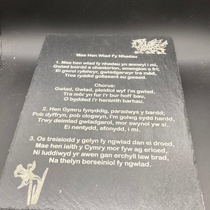 Puede incluir: Una placa de pizarra negra con un poema galés grabado en blanco titulado "Mae Hen Wlad Fy Nhadau" (La Vieja Tierra de Mis Padres). El poema trata sobre el orgullo y el patriotismo galés. La placa presenta un dragón galés grabado en blanco en la parte superior.