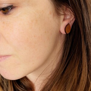 Puede incluir: Un par de pendientes de cuero marrón. Los pendientes son de forma ovalada y tienen una superficie ligeramente texturizada.