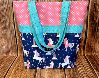 May include: A large tote bag with pink and white polka dot fabric on the top and turquoise fabric in the middle. The bottom of the bag is navy blue with a unicorn and rainbow print.
