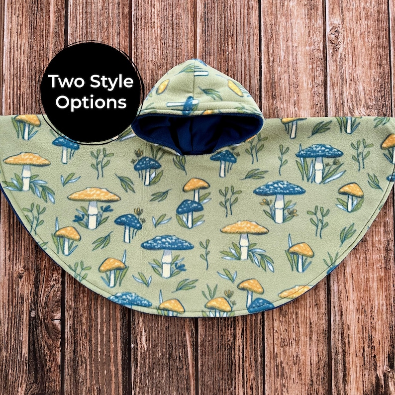 May include: A green fleece poncho with a hood, featuring a pattern of blue and yellow mushrooms and leaves. The hood has a dark blue lining. The text "Two Style Options" is in a black circle. The poncho is displayed on a wooden surface.
