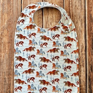 May include: A white bib with a pattern of brown and gray horses running across a white background with cacti.