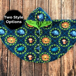 May include: A hooded cape with a jungle animal print. The navy blue fleece cape features a pattern of lions, elephants, monkeys, and other animals. The hood and lining are bright green. The cape has white buttons and the text "Two Style Options" in a black circle.