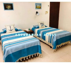 May include: Two twin-sized beds with blue and white striped bedspreads and white fringe. The bedspreads have a nautical theme with an anchor and fish designs. The beds are in a room with white walls and a wooden door.