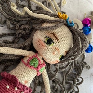 May include: A crocheted mermaid doll with long brown hair, a pink tail, and a green and pink bikini top. The doll has green eyes and a sweet expression.