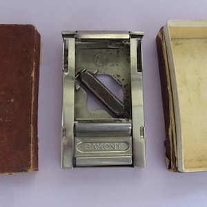 May include: A silver razor blade sharpener with the word "Bakony" printed on the front. The sharpener is open and the blade is visible. The sharpener is in a brown cardboard box.