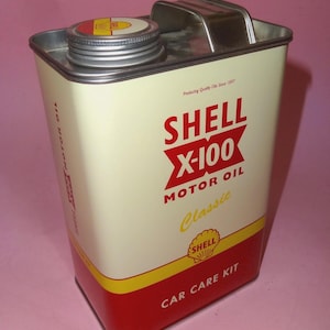 Puede incluir: Lata de aceite de motor Shell X-100 vintage. El recipiente metálico rectangular es de color crema con detalles rojos y amarillos. El logotipo de Shell y "X-100 Motor Oil Classic" se muestran de forma destacada. La lata también dice "Car Care Kit".