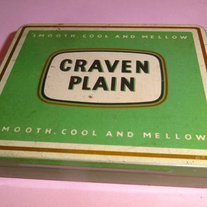 Może przedstawiać: Metalowe pudełko na papierosy w kolorze zielonym i złotym z napisem "Craven Plain" i frazą "Smooth. Cool and Mellow" na przodzie.