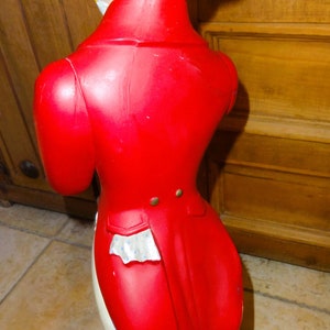 May include: A red and white figurine of a person wearing a top hat and a red coat with a tailcoat. The figurine is standing on a red base.