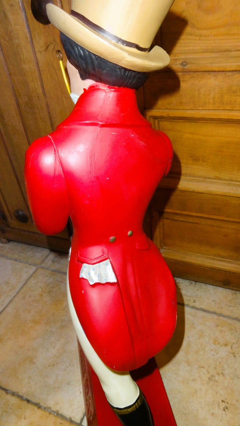 May include: A red and white figurine of a person wearing a top hat and a red coat with a tailcoat. The figurine is standing on a red base.
