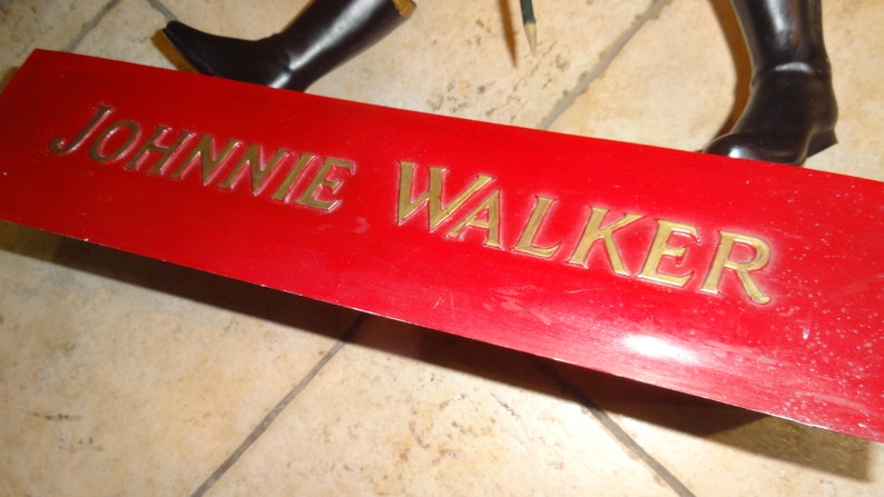 May include: A red metal sign with the words "JOHNNIE WALKER" in gold lettering.