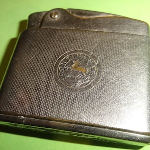 May include: Silver lighter with a textured surface and a circular logo featuring a stylized horse and the text "Continental".