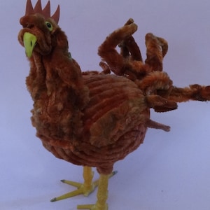 Peut inclure: Un poulet en cure-pipe brun avec des pattes jaunes et un bec vert. Le poulet est fait de cure-pipes et a une texture moelleuse.