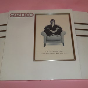 May include: A white framed advertisement for Seiko watches featuring a woman sitting in a chair with the text "It's your watch that tells more about who you are."
