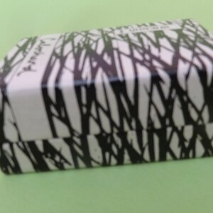 May include: A rectangular box with a white background and a black tree branch pattern. The box has a hinged lid and a white vertical stripe on the front. The box is on a light green surface.