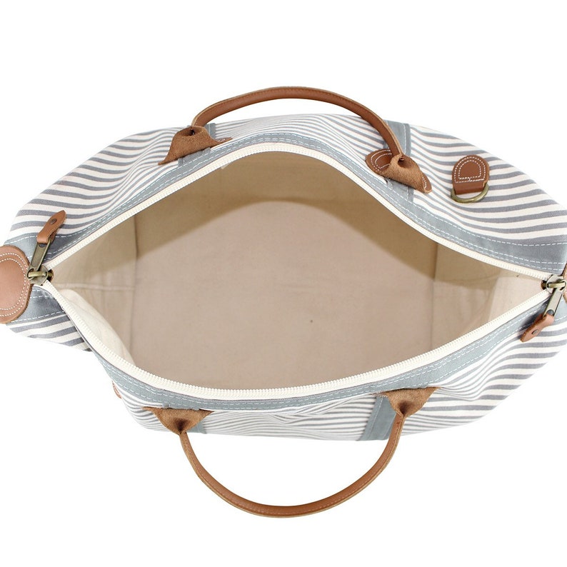 May include: A striped canvas travel bag with brown leather handles and accents. The bag is open and the interior is visible.