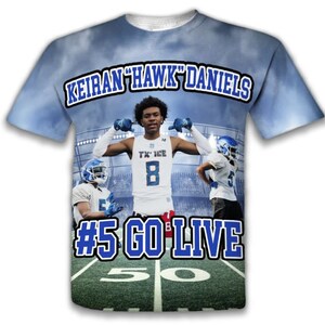 May include: A blue and white t-shirt with a football player on the front. The shirt has the text "Keiran "Hawk" Daniels #5 Go Live" on the front.