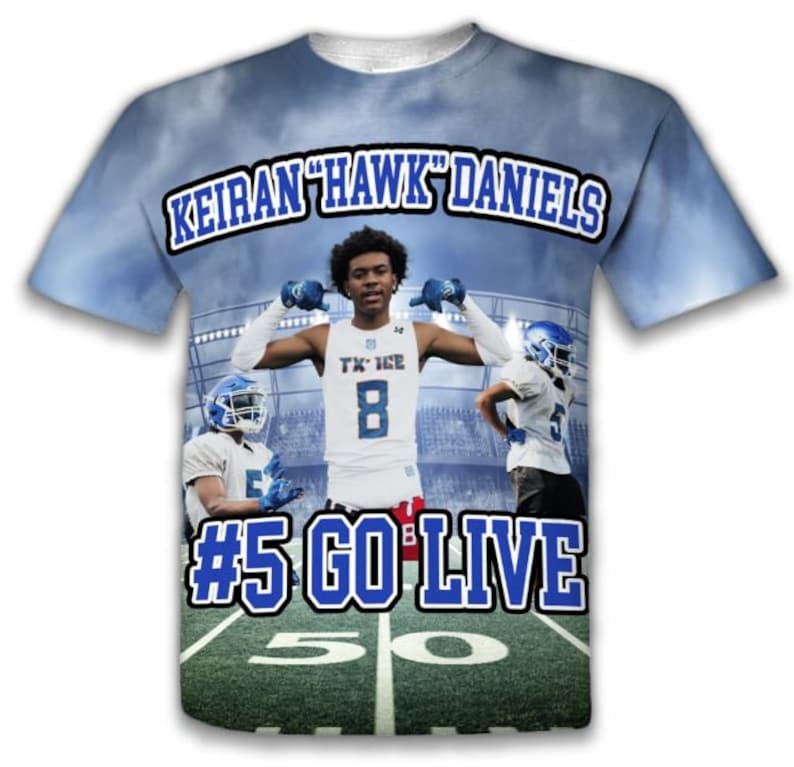 May include: A blue and white t-shirt with a football player on the front. The shirt has the text "Keiran "Hawk" Daniels #5 Go Live" on the front.
