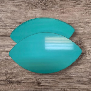May include: Two turquoise, leaf-shaped wooden serving platters are arranged on a wooden surface. The platters have a glossy finish and are slightly overlapping. The wood grain background provides a natural contrast to the vibrant color of the platters.
