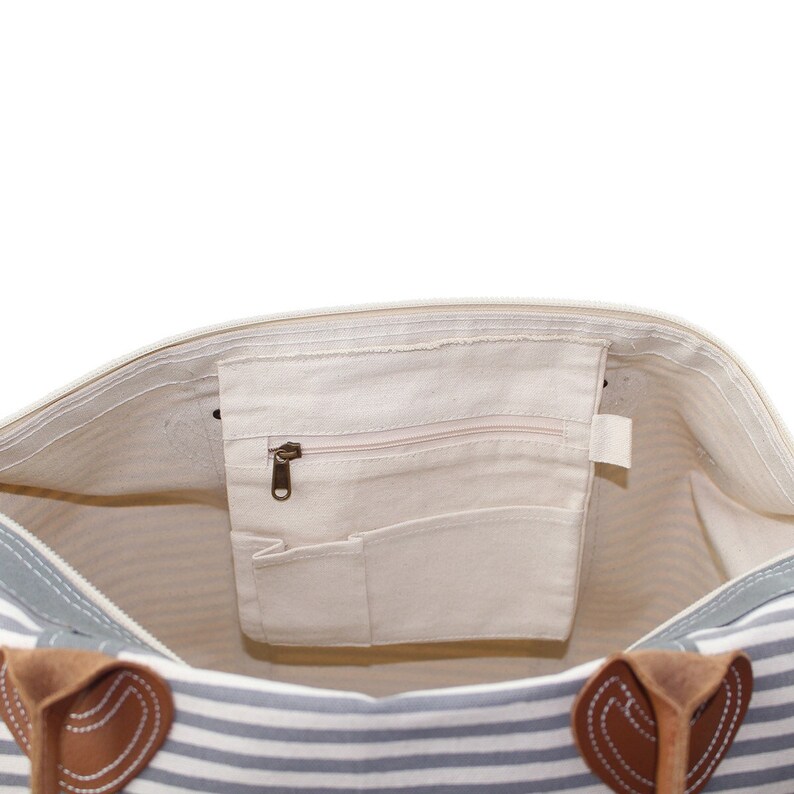 May include: Inside view of a striped tote bag with a zipped pocket and two leather handles. The bag is lined with a cream-coloured fabric.