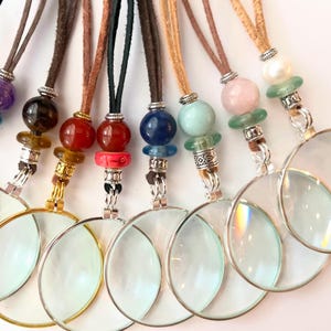 May include: A collection of magnifying glasses on leather cords, each with a different colored bead accent. The magnifying glasses have silver or gold-colored frames. The beads are various colors, including red, blue, and green.