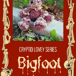 Op de afbeelding: Een handgemaakte, pluche Bigfoot-pop in tinten bordeauxrood en bruin, met zwarte knoopogen. De pop maakt deel uit van de "Cryptid Lovey Series" van CozyCrochetCreations. De afbeelding is omlijst met een decoratieve rand van botten.