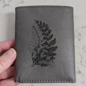 Cartera TLOU: símbolo de las luciérnagas o tatuaje de Ellie, grabado con láser en una cartera de tres pliegues de cuero sintético gris. The Last of Us