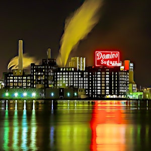 May include: A nighttime view of a large industrial building with a red neon sign that reads "Domino Sugars". The building is illuminated by lights and there is smoke coming from the chimney.