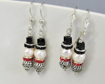 May include: A pair of silver dangle earrings featuring black, white and red beads. The beads are arranged to resemble a snowman.