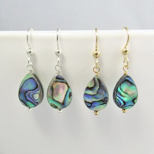 May include: Four teardrop-shaped abalone shell earrings with iridescent blue, green, and purple patterns. Two earrings feature silver-toned metal hooks and findings, while the other two feature gold-toned metal hooks and findings, all hanging vertically.