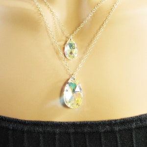 Pu&ograve; includere: Una collana a catena d'argento a pi&ugrave; strati con tre ciondoli di cristallo a forma di goccia. I cristalli sono trasparenti e iridescenti.