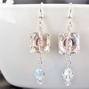 May include: A pair of silver dangle earrings with clear crystal square and round stones.