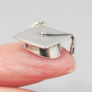 May include: A silver graduation cap charm with a tassel. The charm is small and detailed, perfect for adding a touch of personalization to a necklace or bracelet.