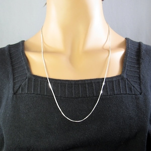 May include: A silver chain necklace on a mannequin. The chain is thin and delicate.