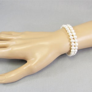 May include: Two bracelets made of white pearls on a mannequin wrist.