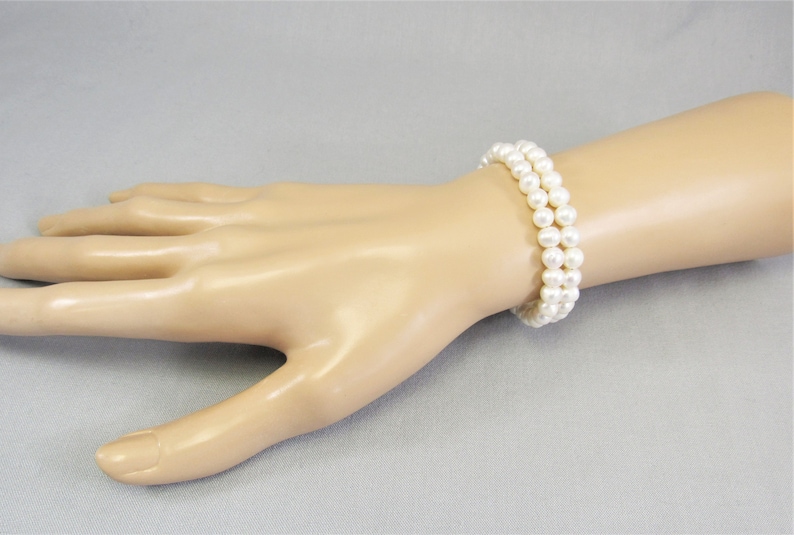 May include: Two bracelets made of white pearls on a mannequin wrist.