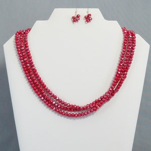 May include: A red crystal necklace and matching earrings. The necklace is made of multiple strands of small, faceted beads. The earrings are small and dangle.