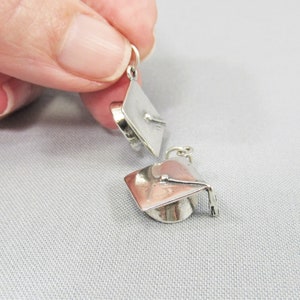May include: Two silver graduation cap charms. The charms are small and detailed, with a tassel and a graduation cap.