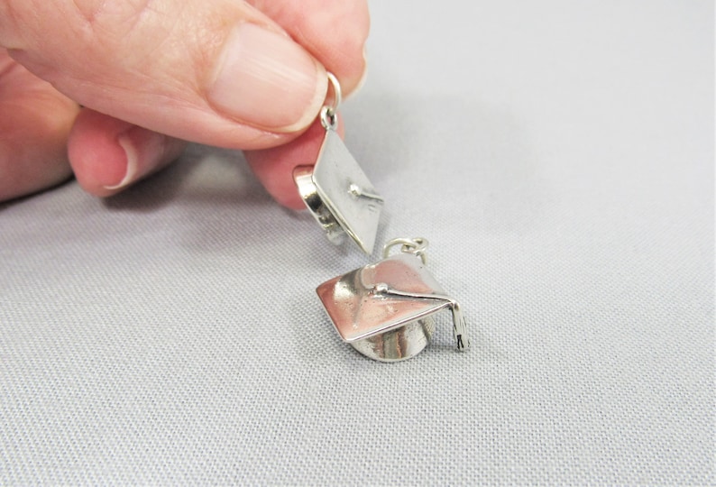 May include: Two silver graduation cap charms. The charms are small and detailed, with a tassel and a graduation cap.