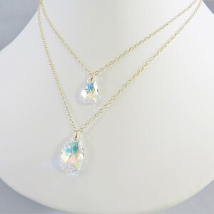 Pu&ograve; includere: Una collana a catena dorata con due ciondoli a forma di goccia di cristallo. I cristalli sono iridescenti e hanno un effetto arcobaleno.