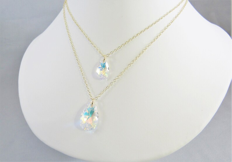 Pu&ograve; includere: Una collana a catena dorata con due ciondoli a forma di goccia di cristallo. I cristalli sono iridescenti e hanno un effetto arcobaleno.