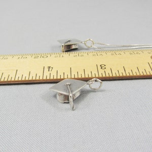 May include: Two silver graduation cap charms on a ruler. The charms are about 1 inch in size.