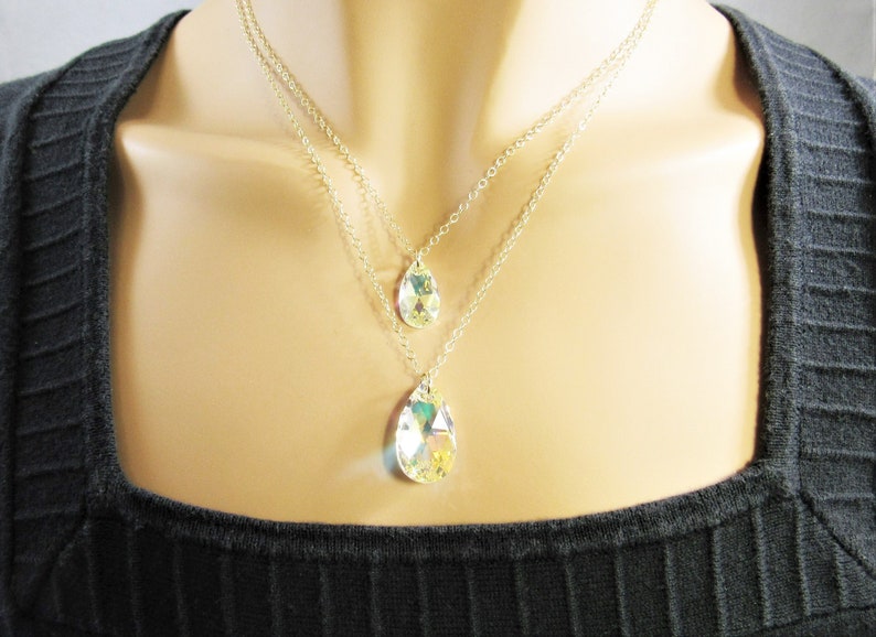 Pu&ograve; includere: Una collana a catena d'argento a pi&ugrave; strati con tre ciondoli di cristallo a forma di goccia. I cristalli sono trasparenti e iridescenti.