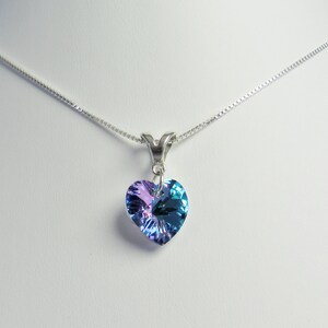 May include: A silver necklace with a heart-shaped pendant. The pendant is a gradient of blue and purple hues. The necklace is displayed on a white surface.
