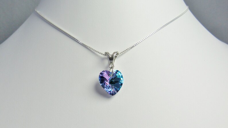 May include: A silver necklace with a heart-shaped pendant. The pendant is a gradient of blue and purple hues. The necklace is displayed on a white surface.