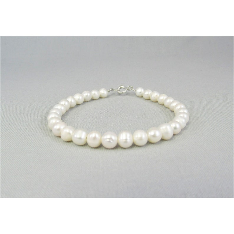 May include: A white pearl bracelet with a silver clasp lies on a grey cloth background. The freshwater pearls are 5.5 to 6 mm in size and potato or off-round in shape. They have a nice luster with some having natural seams.
