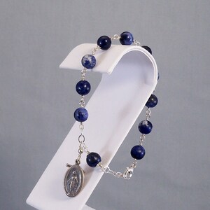 May include: A silver chain bracelet with blue and white beads and a silver charm of the Virgin Mary.