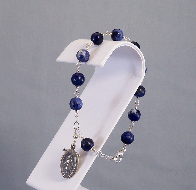 May include: A silver chain bracelet with blue and white beads and a silver charm of the Virgin Mary.