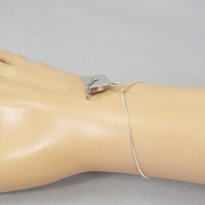 May include: A silver graduation cap charm on a silver chain bracelet. The bracelet is on a mannequin's wrist.