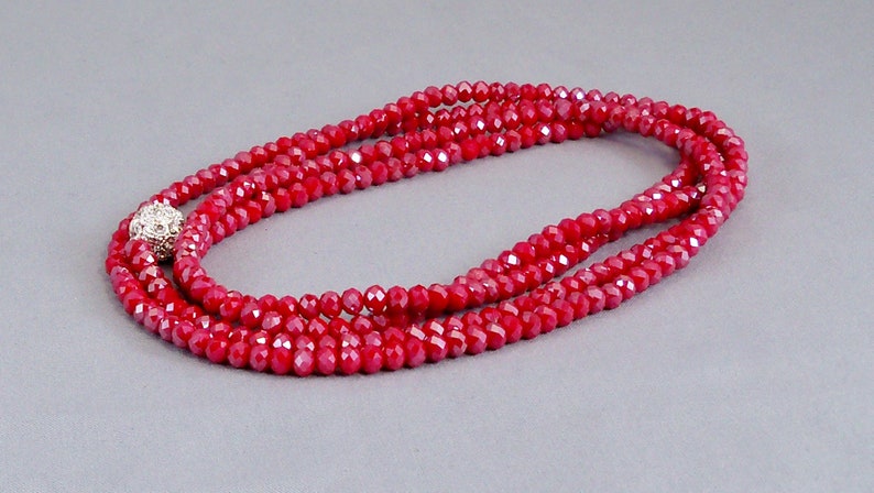 May include: A red crystal bead necklace with a silver-toned bead accent. The necklace is layered and has a shiny finish.